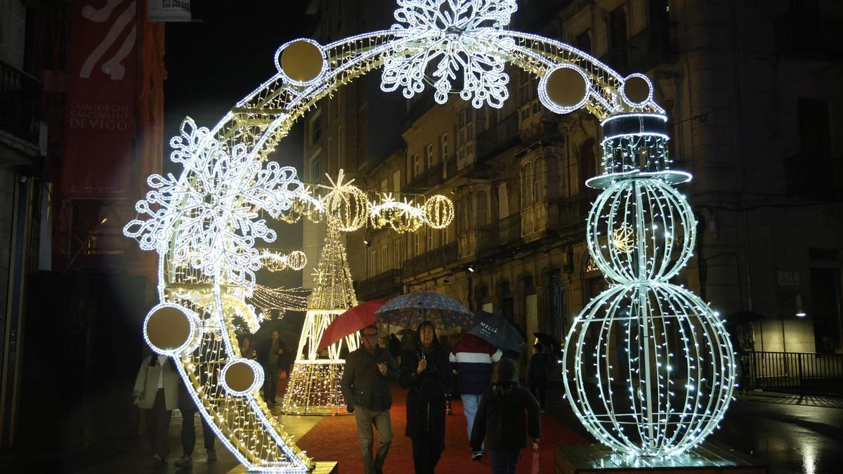 Personas paseando por el centro de Vigo, iluminado con las luces de Navidad.
