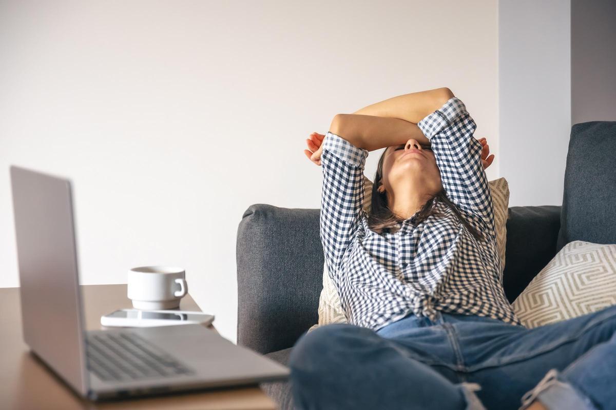 Tired from work, a young woman with a laptop lies on the couch.