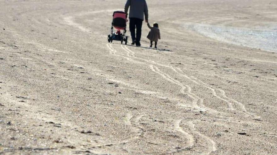 Un hombre camina con una niña por una playa gallega.