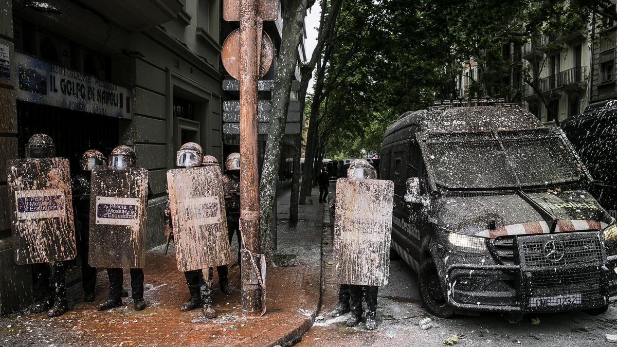 Agentes y furgones de los Mossos d'Esquadra, repletos de pintura durante el desalojo del bloque Llavors en 2021, en Barcelona.