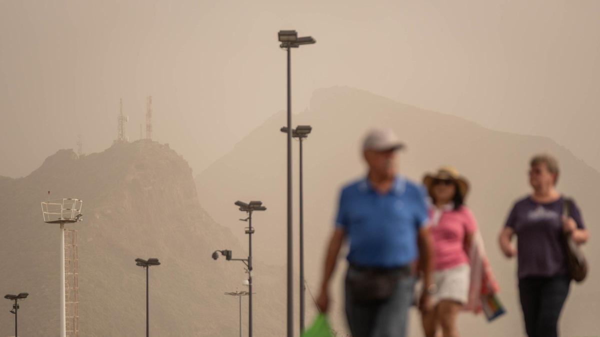 Varias personas pasean por el centro de Santa Cruz de Tenerife. En el fondo, el macizo de Anaga completamente emborronado por la calima.
