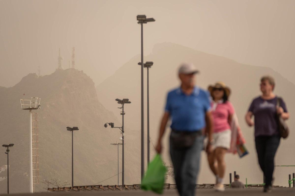 Varias personas pasean por el centro de Santa Cruz de Tenerife. En el fondo, el macizo de Anaga completamente emborronado por la calima.