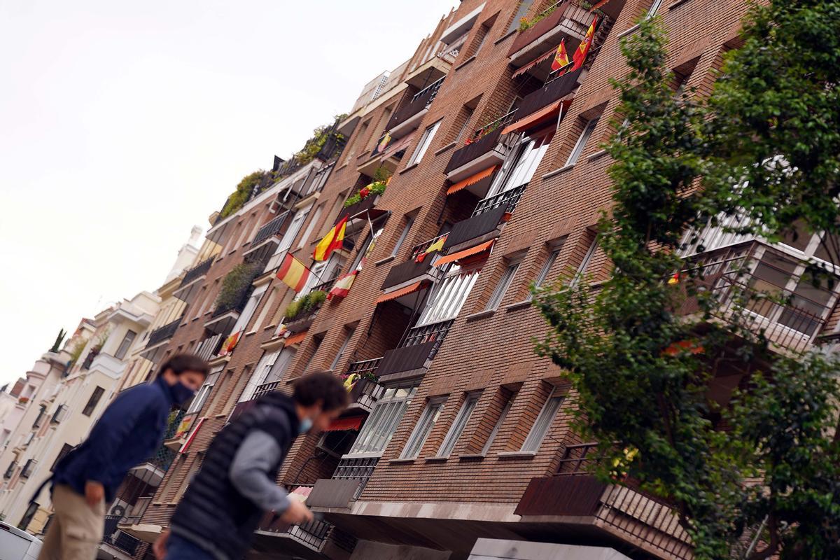 Dos vecinos pasan bajo un edificio decorado con banderas de España en la calle Núñez de Balboa, del distrito madrileño de Salamanca. 