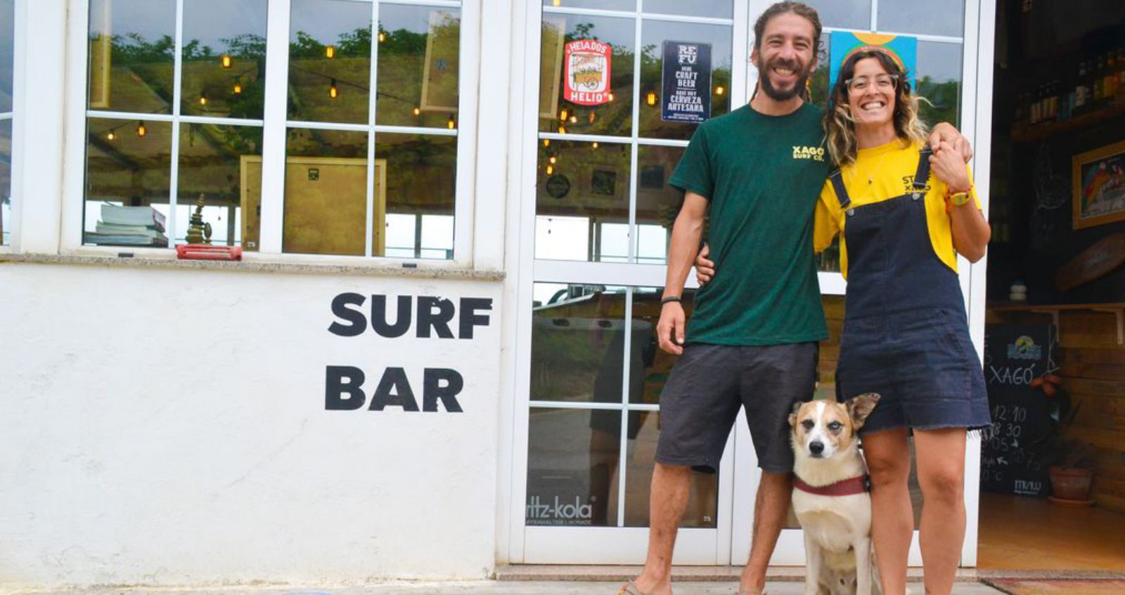 Enol Valles y Sofía Lacheta, a la entrada de su local, Xagó Surf Co, con su perro.  | A. P. Paredes 