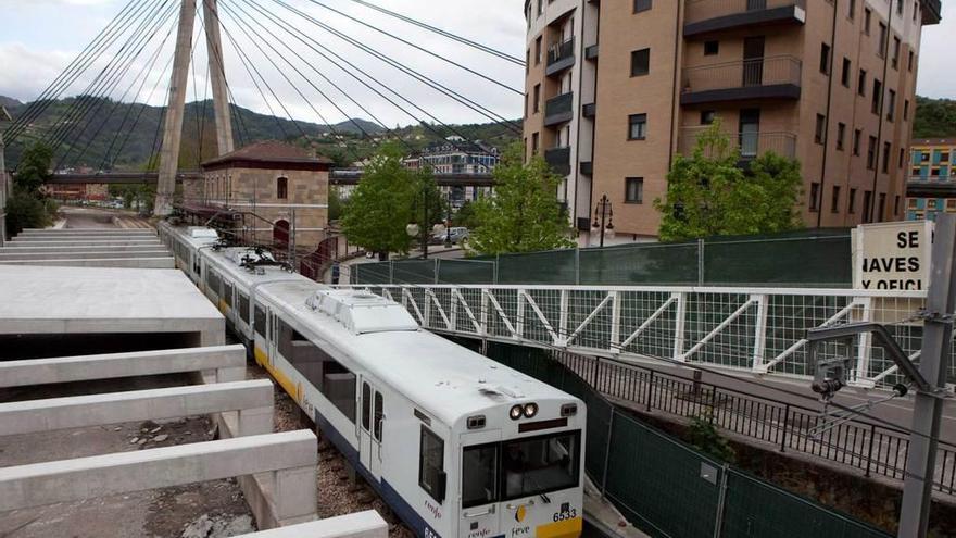 Un tren de Feve circula por Langreo, con la obra del falso túnel del soterramiento a la izquierda.