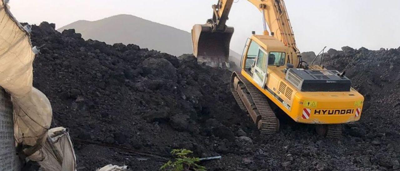 Una retroexcavadora trabaja en una de las zonas de coladas por donde discurre el trazado de la carretera de la costa.