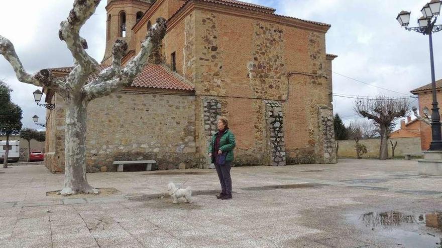 Una mujer pasea con su perro en la plaza de la iglesia de Santa Cristina de la Polvorosa.