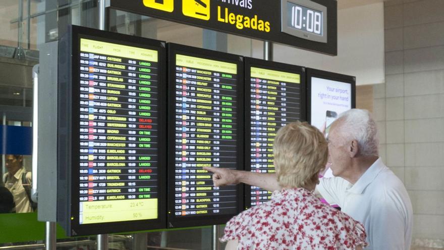 Dos personas mayores miran los paneles informativos del aeropuerto de Alicante. | L.O.