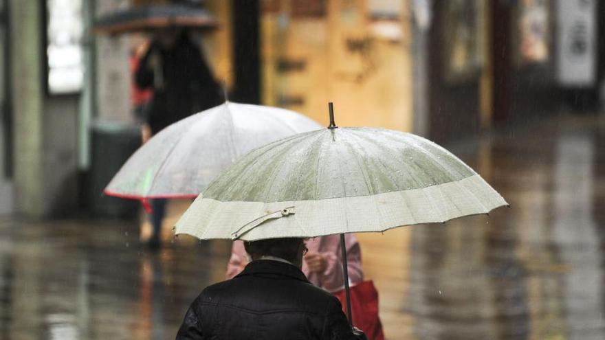 Un viandante pasea con paraguas por la calle Real.