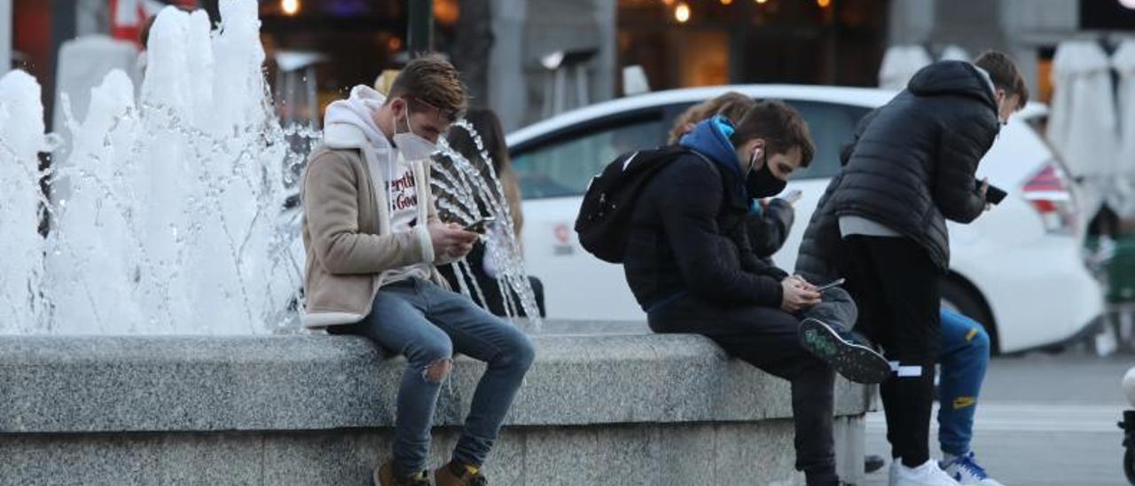 Varios jóvenes en la fuente de la plaza España de Zaragoza con sus teléfonos móviles.  | ÁNGEL DE CASTRO