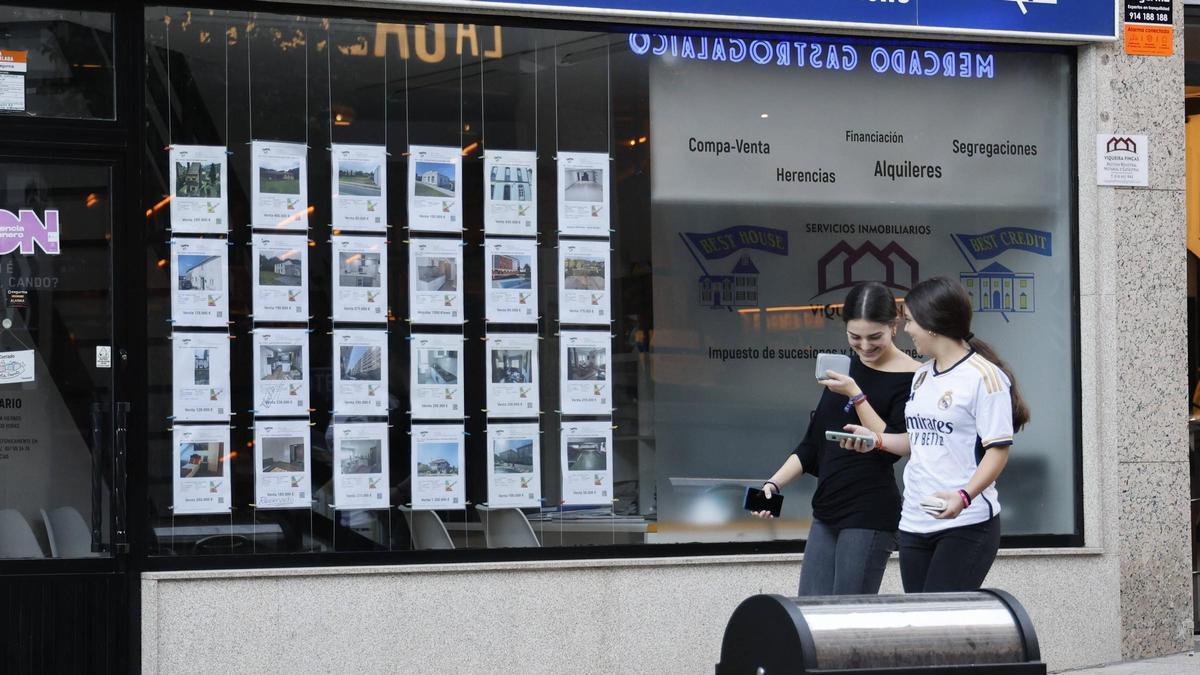 Dos jóvenes pasan por delante de una inmobiliaria en Compostela.