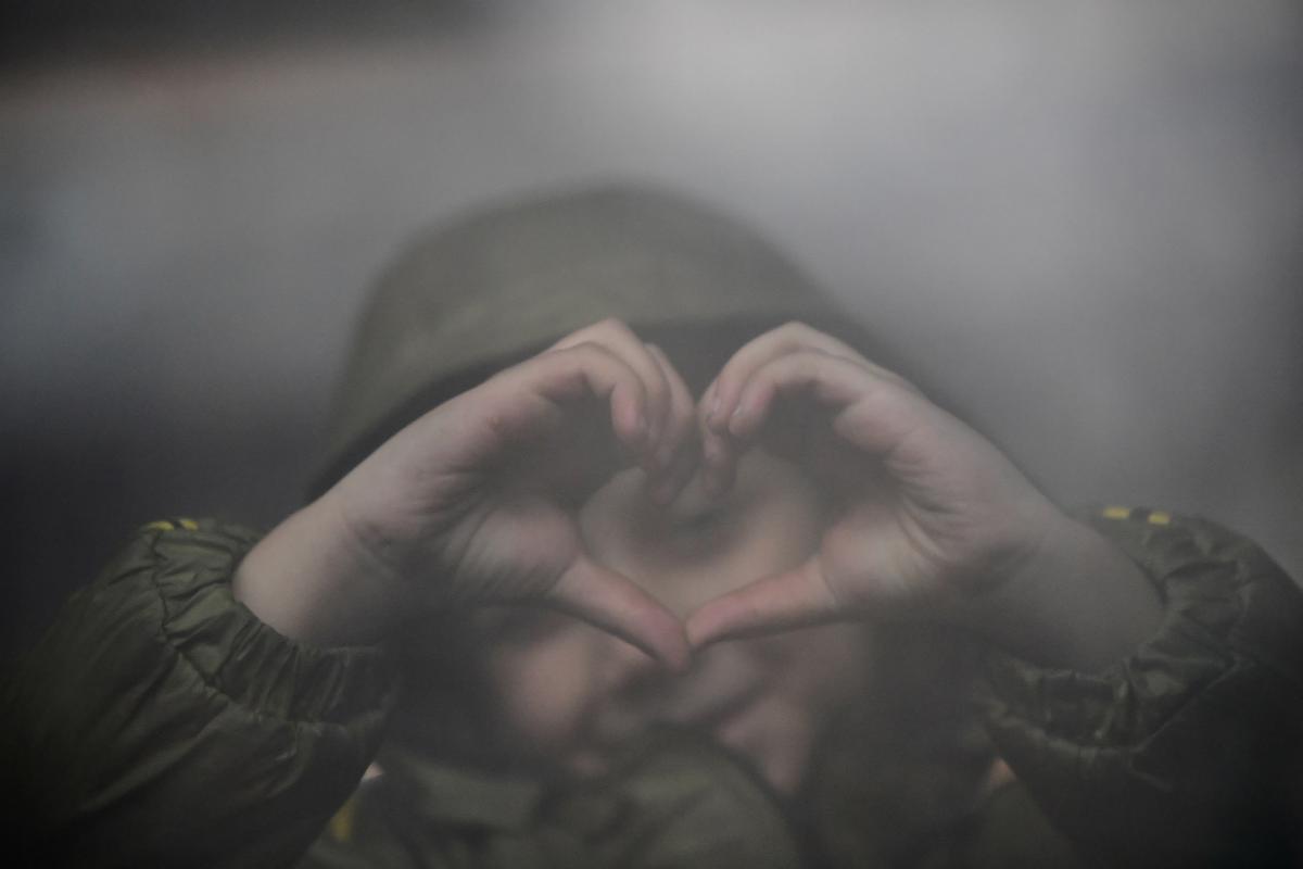 Una niña refugiada forma una corazón con las manos mientras espera en una estación de Hungría.