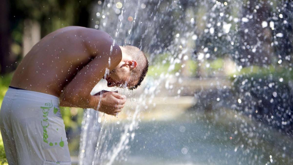 Un joven sin camiseta se refresca en una fuente