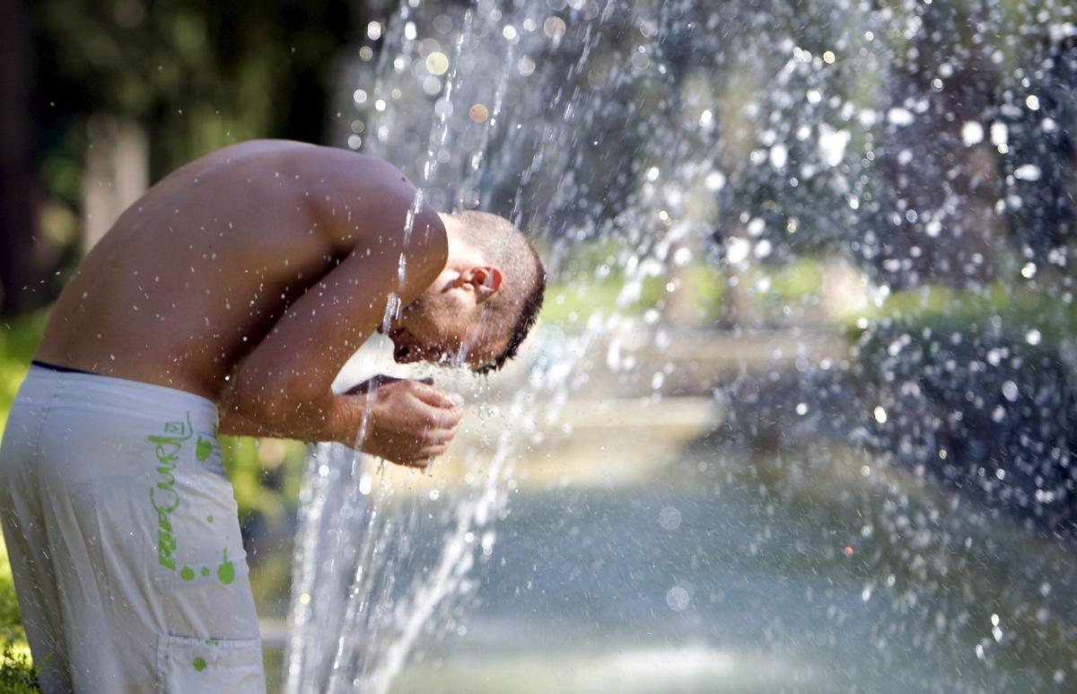 Un joven se refresca en una fuente del parque de María Luisa de Sevilla.