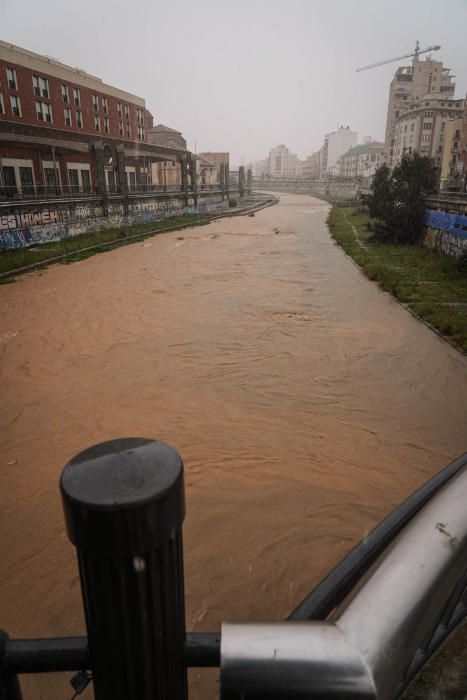 El río Guadalmedina crecido con agua y calles del Centro y el entorno del cauce, desiertas bajo la lluvia, la estampa de este martes 31 de marzo.