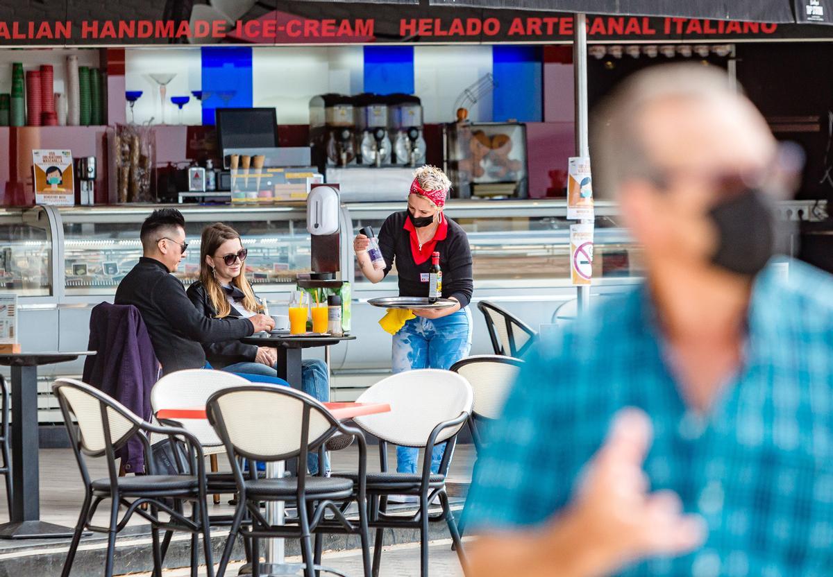 Una camarera sirve a dos clientes en una terraza de Alicante
