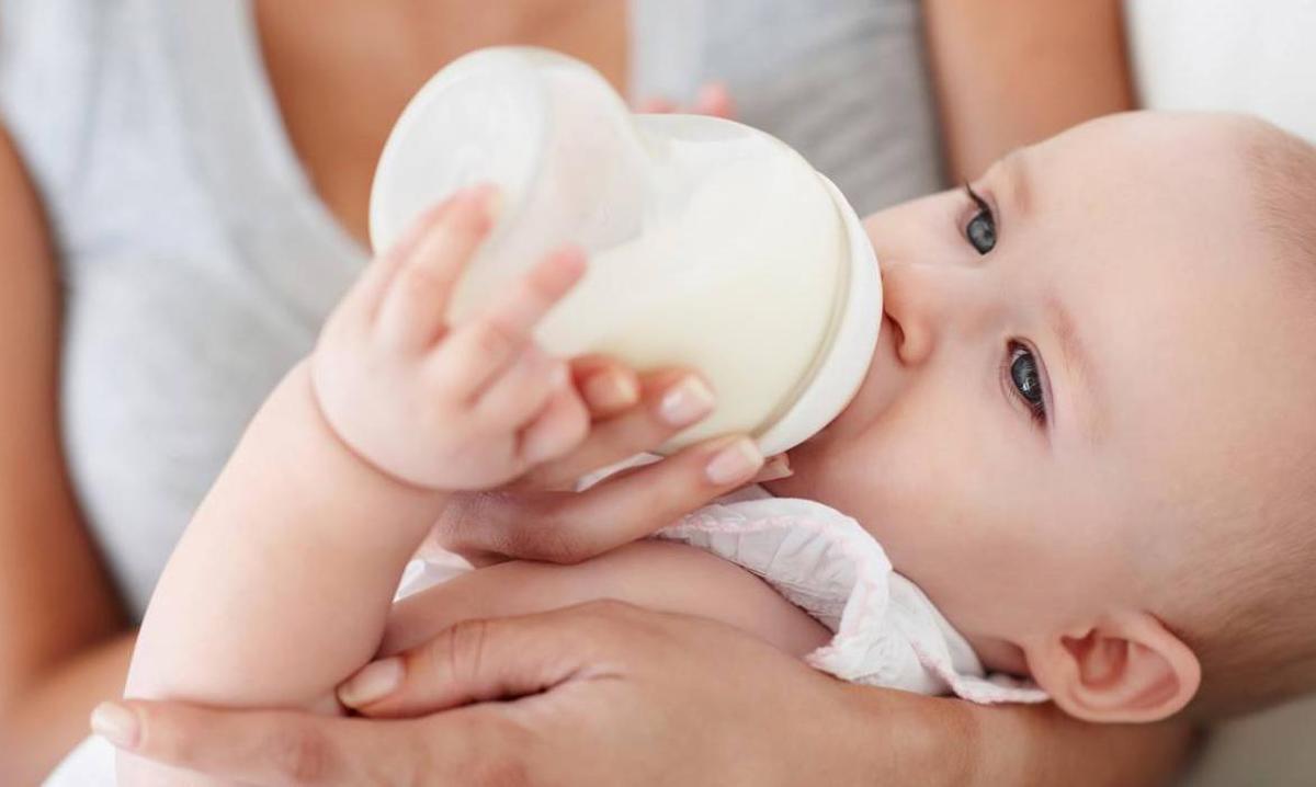 Un bebé toma leche de fórmula en brazos de su madre.
