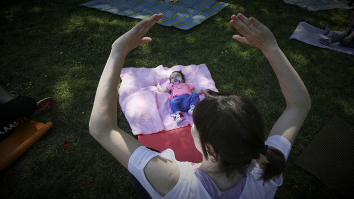 Una madre, con su bebé, hace gimnasia en un parque de Barcelona.