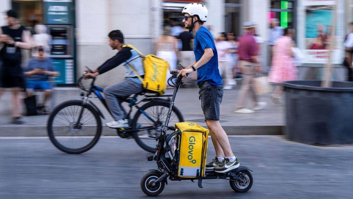Dos repartidors de Glovo, un en bicicleta i un altre en patinet, entreguen les seves comandes a Barcelona. | ZOWY VOETEN
