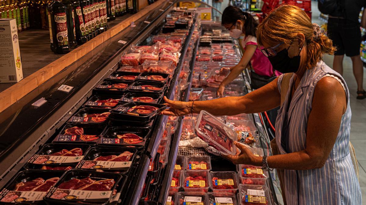 Una mujer examina varios paquetes de carne envasada en un mercado.