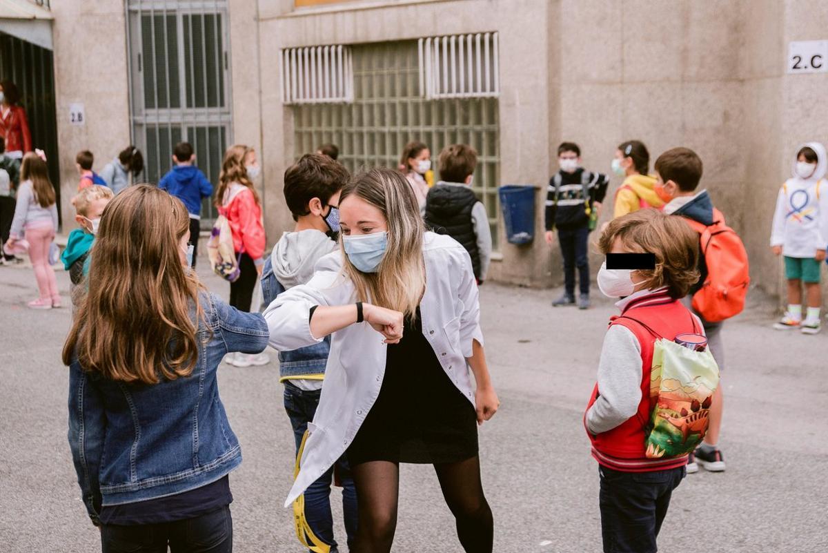 Profesora saludando con el codo a los alumnos.