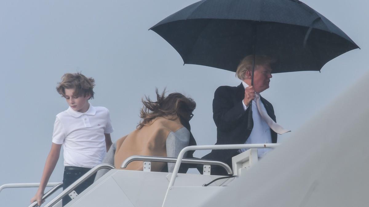 El presidente de EEUU, Donald Trump, sostiene un amplio paraguas para protegerse de la lluvia, mientras espera a su mujer Melania y a su hijo Barron, durante el embarque del Air Force One en Flordia.