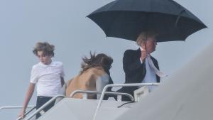 El presidente de EEUU, Donald Trump, sostiene un amplio paraguas para protegerse de la lluvia, mientras espera a su mujer Melania y a su hijo Barron, durante el embarque del Air Force One en Flordia. 