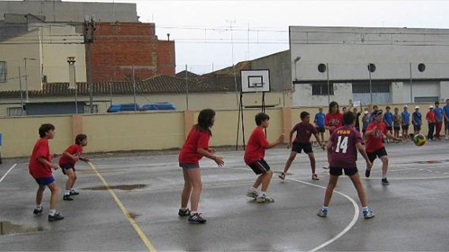 Un partit de colpbol al pati de d&#039;una escola. Dos equips de set xiques i xics mesclats competeixen per introduir el baló a la porteria contrària a base de colps de mà.