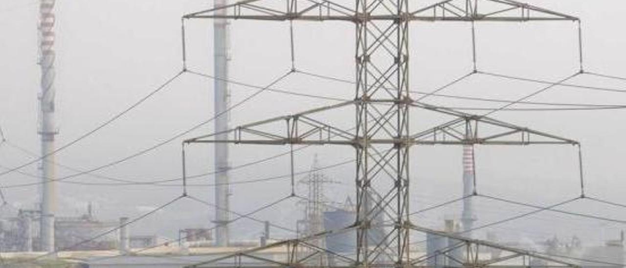 Una torre eléctrica con la planta de Asturiana de Zinc al fondo.