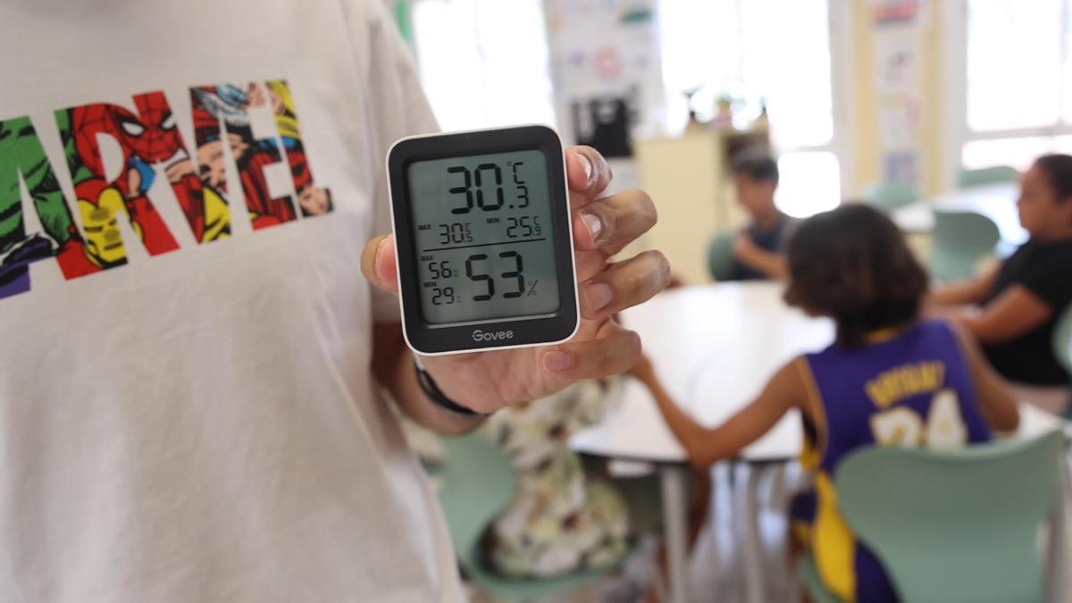 Una persona sostiene un termómetro que marca 30 grados en el interior de un aula.