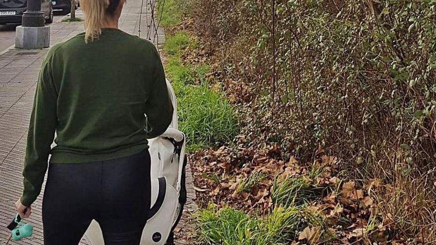 La presidenta de la asociación de vecinos, paseando a su bebé junto a una de las parcelas tomadas por la maleza.