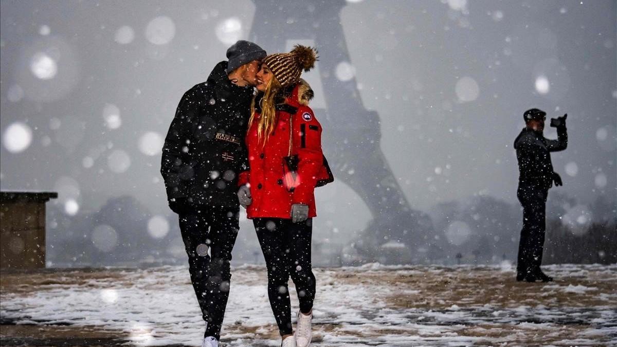 Una pareja se hace carantoñas bajo la mirada de la Torre Eiffel, mientras la nieve cae sobre París.