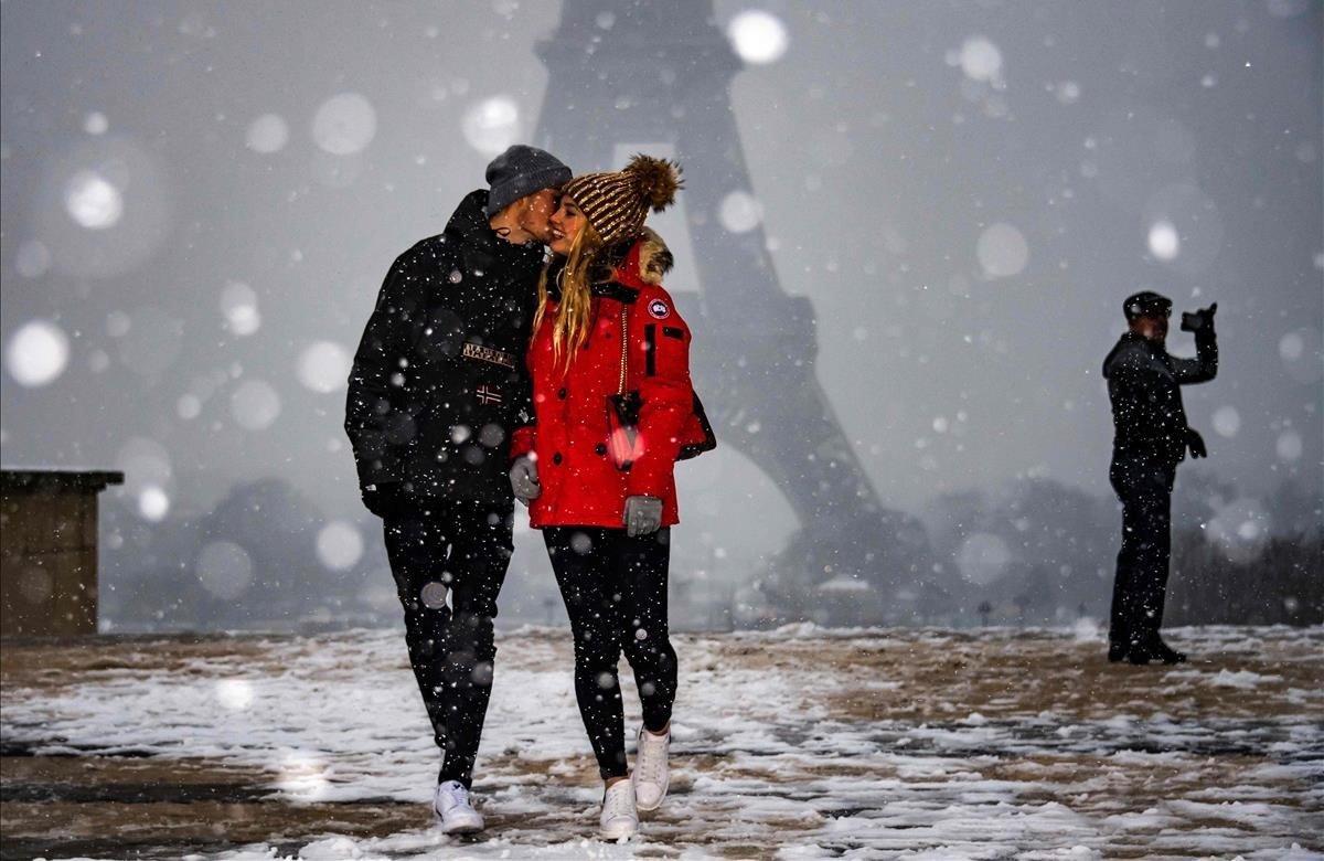 Una pareja se hace carantoñas bajo la mirada de la Torre Eiffel, mientras la nieve cae sobre París.