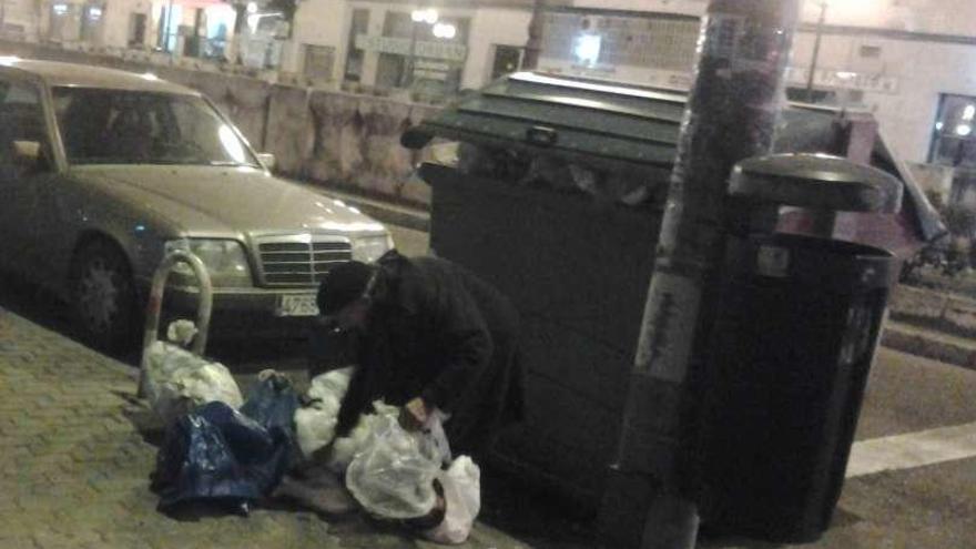 Una persona recoge bolsas junto a un contenedor en Tres Cruces.