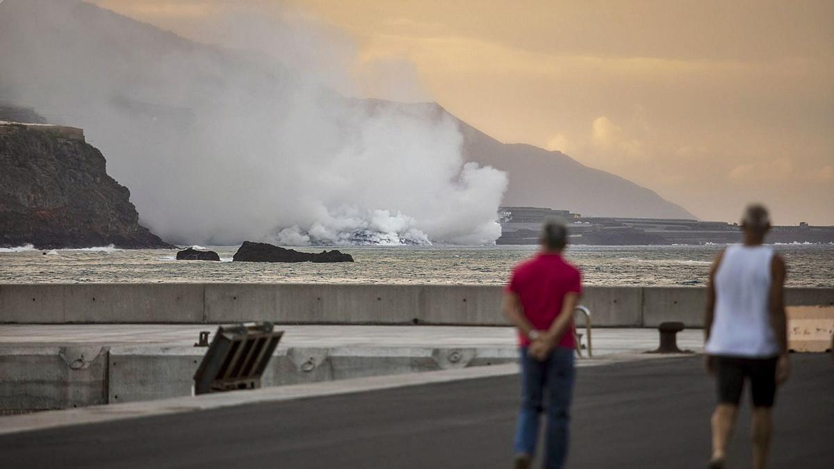 Dos personas observan desde el puerto de Tazacorte la columna de humo que despide la lava cuando entra en contacto con el mar.