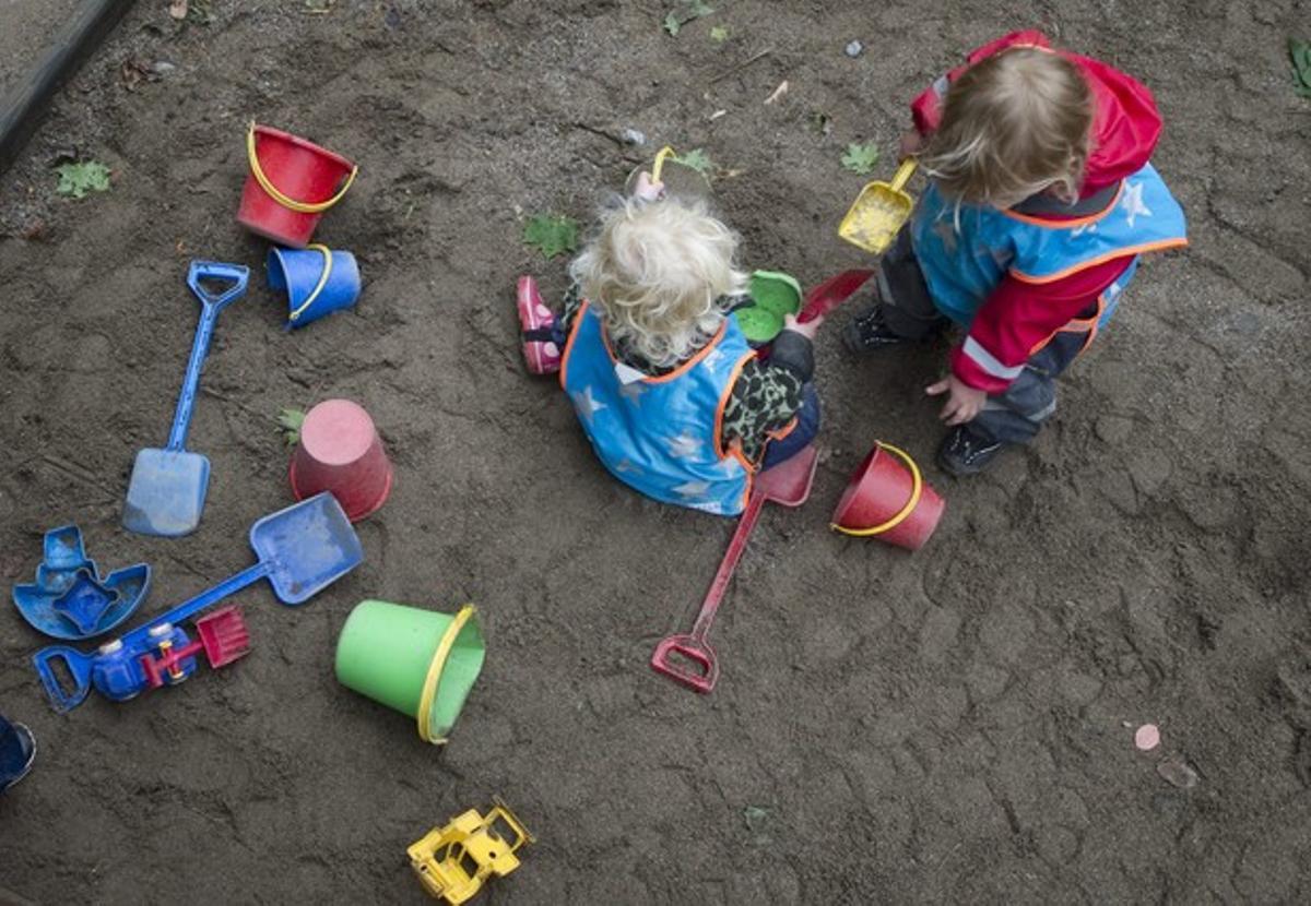 Dos niños juegan con la arena en el patio de una guardería.