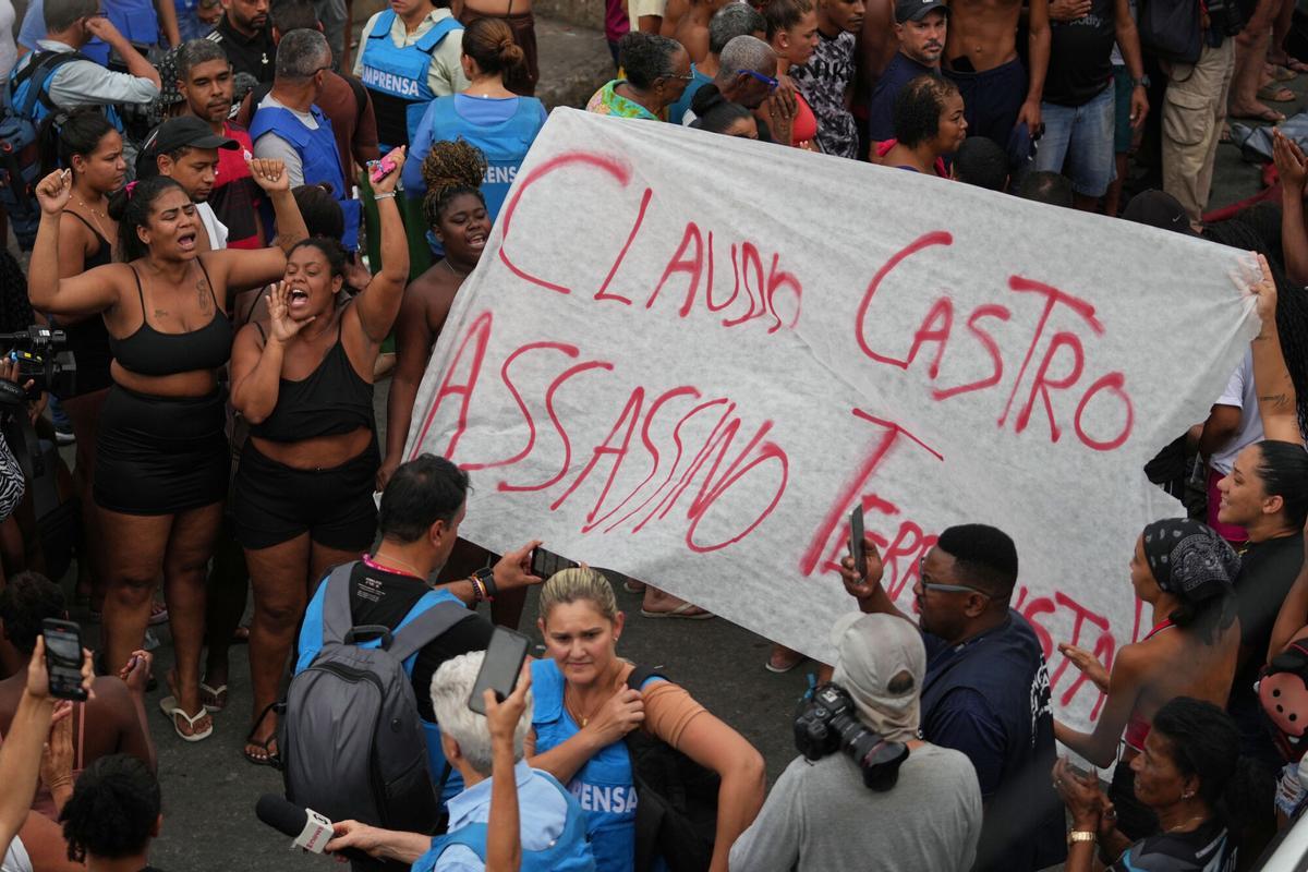 Protesters display a banner reading in Portuguese Claudio Castro Murderer, referring to Rio de Janeiro state Governor Claudio Castro, a day after a deadly police raid targeting the Comando Vermelho gang in the Complexo da Penha favela of Rio de Janeiro, Brazil, Wednesday, Oct. 29, 2025. (AP Photo/Silvia Izquierdo)