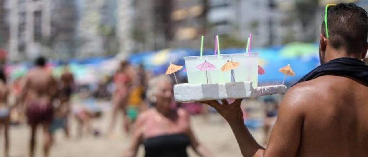 Un vendedor ambulante sostiene una bandeja llena de cócteles en la playa de Benidorm.