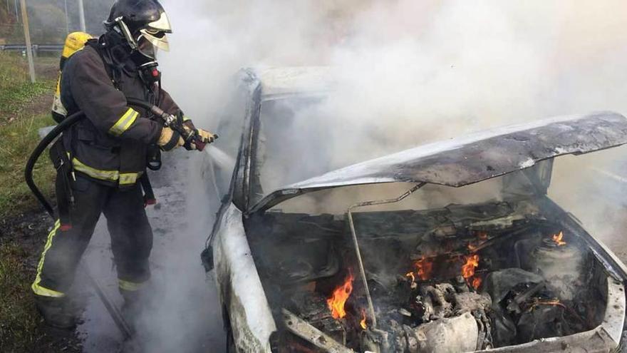 Un bombero apaga el fuego del coche en Villaviciosa.