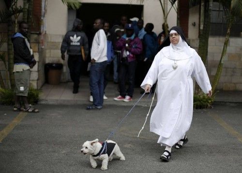 A nun walks her dog past Haitian immigrants at the Nossa Senhora da Paz Catholic church, where the immigrants are staying in a shelter, in Sao Paulo