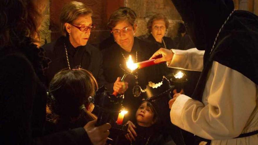 Un cerillero prende las velas de varias hermanas vestidas de luto.