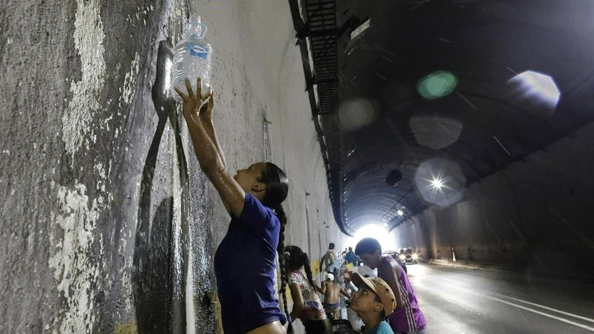 Una mujer recoge agua de una fuga en una tubería en el túnel de una autopista en Caracas.