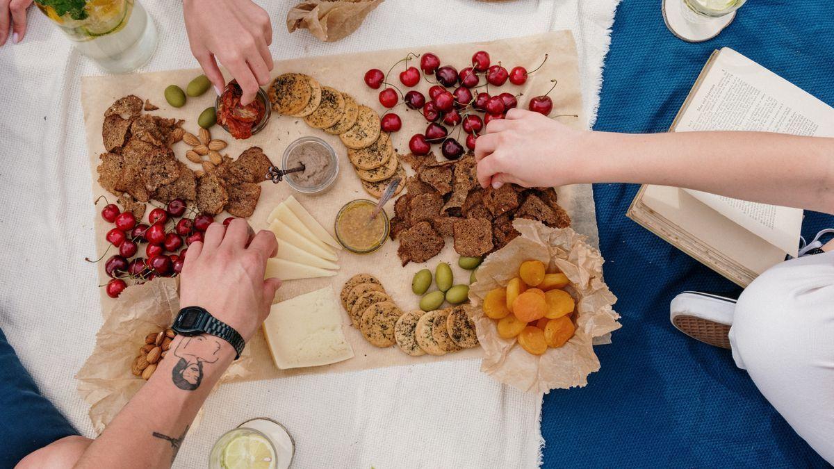 Varias personas cogen diversos alimentos expuestos sobre una bandeja.