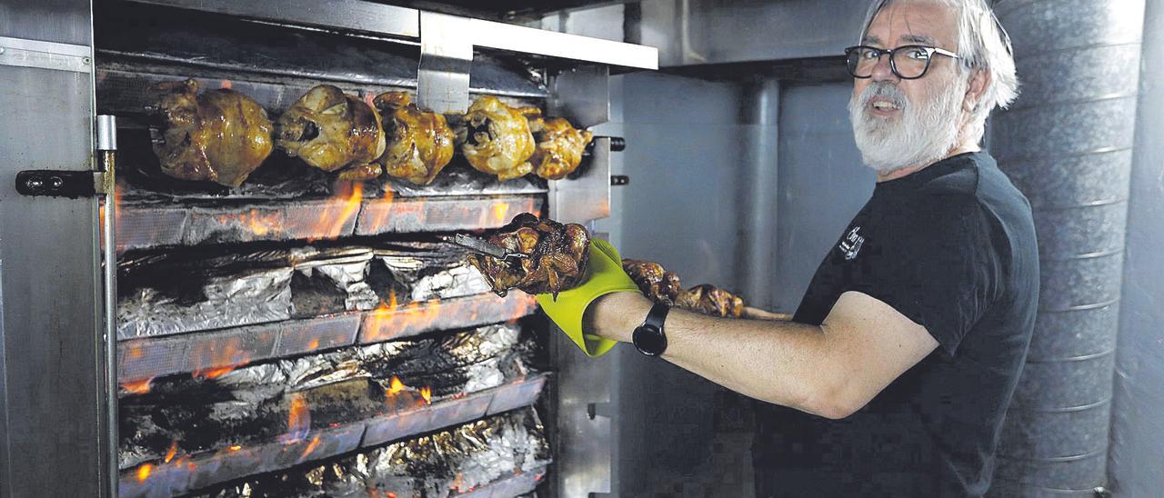 El cocinero de Pollos Vela, una tienda de comidas para llevar de Zaragoza, sacando los pollos recién hechos para servir a sus clientes del día.