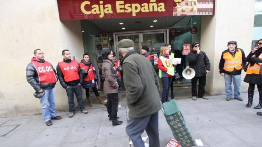 Un hombre pasa frente a varios miembros de CC OO y UGT frente a la oficina de Caja España en Santa Clara.