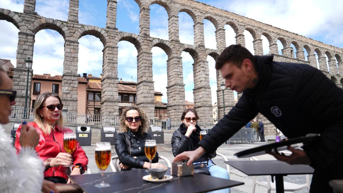 Un camarero atiende una mesa en un bar restaurante frente al acueducto de Segovia.