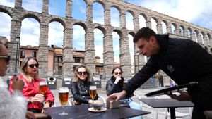 Un camarero atiende una mesa en un bar restaurante frente al acueducto de Segovia.