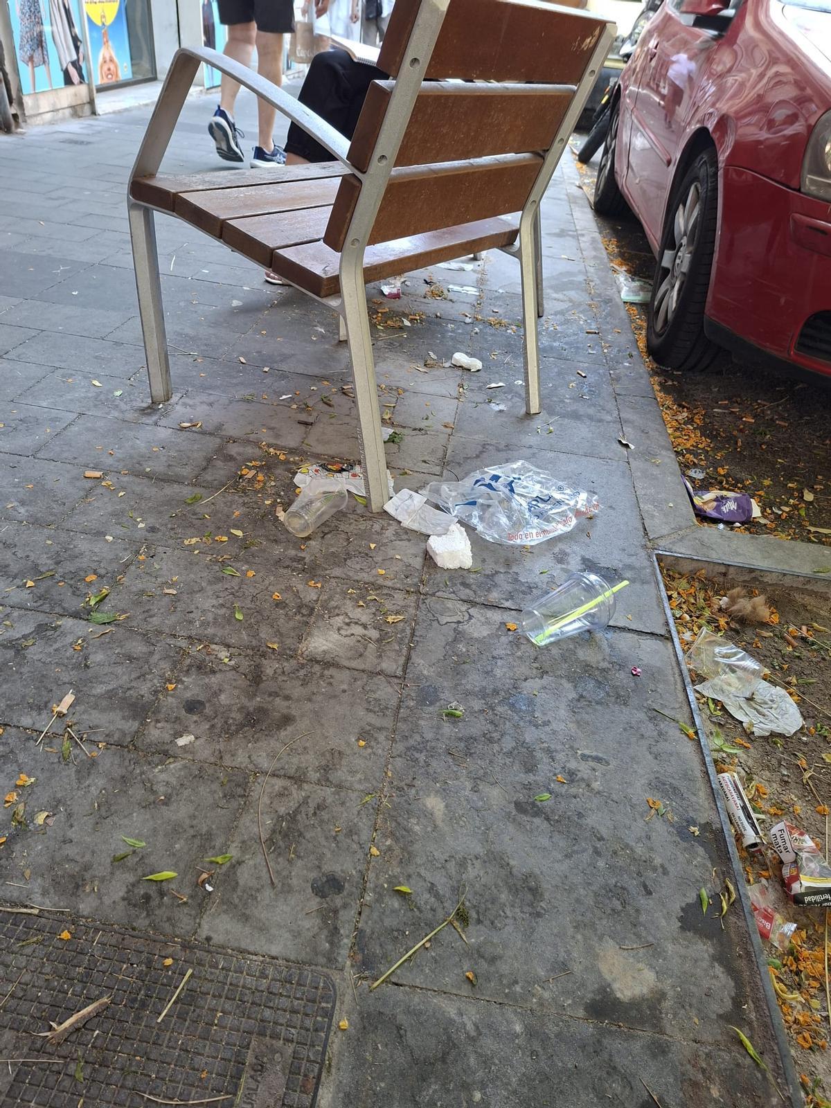 Residuos y envases esparcidos por la acera junto a uno de los bancos de la zona