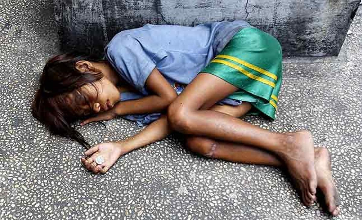 Una nena dorm al carrer amb una moneda a la mà a Manila (Filipines).