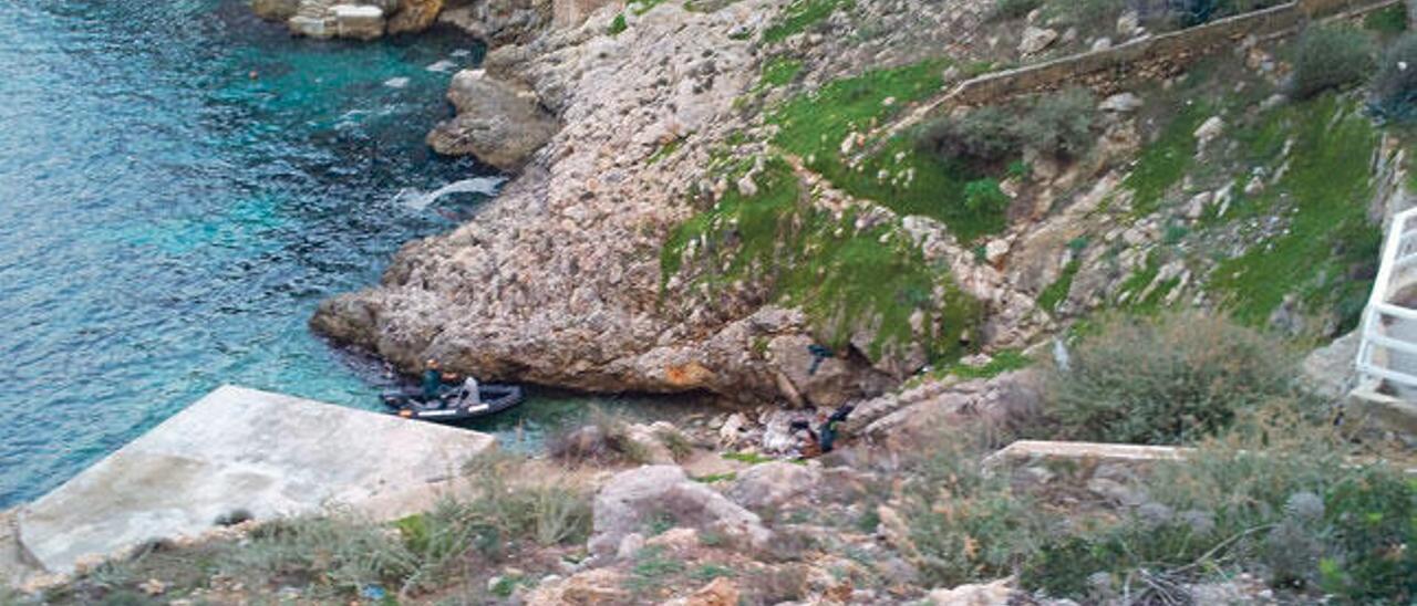 Guardias civiles, con una lancha, analizan el cadáver descubierto sobre unas rocas en la cala.